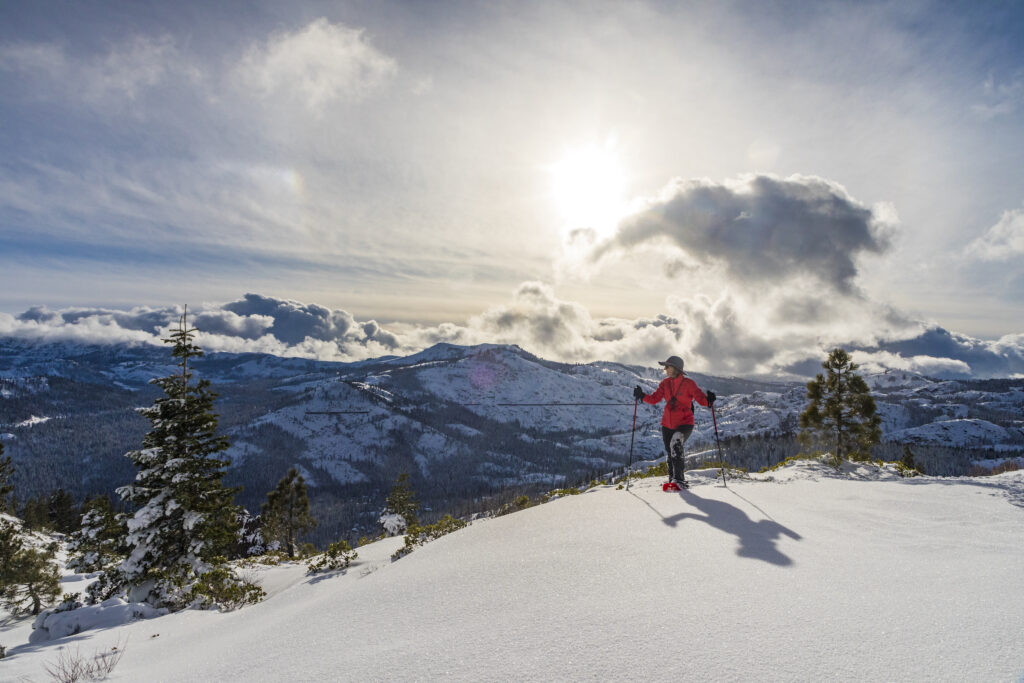 person snowshoeing over Donner Summit overlooking the peaks of the Sierra Nevada on a sunny partly cloudy day