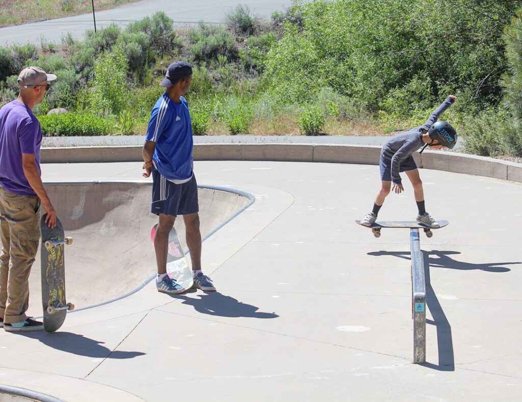 Kid doing a backside boardslide at the Truckee Skatepark while two skateboarders watch
